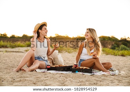 Two young caucasian happy women sitting and smiling while having picnic on beach