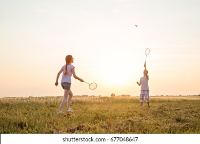 Two young caucasian kids playing badminton in the field at summer sunset