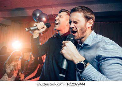 Two Young Caucasian Men In T-shirts Singing In Microphone In Karaoke Bar, Having Fun, Celebrating. Holiday, Leisure, Party Concept