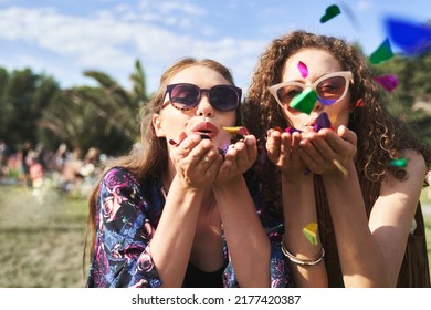 Two Young Caucasian Women Blowing Confetti Towards Camera On Music Festival