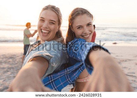 Two young Caucasian women share a joyful moment on the beach. Their laughter and camaraderie embody the essence of carefree youth and friendship.