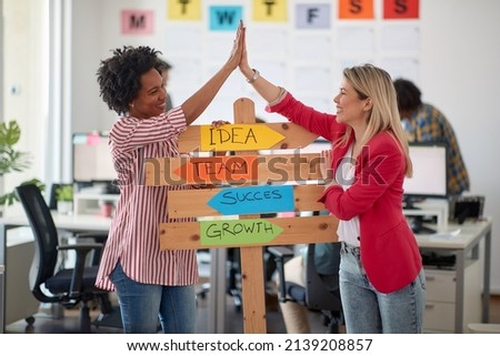 Two young cheerful female office worker are having a good time while posing for a photo and promoting company slogans in a pleasant atmosphere in the office. Employees, job, office