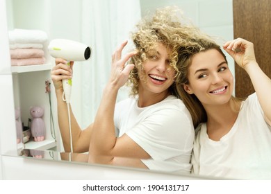 Two young and cheerful women using hairdryer in the bathroom - Powered by Shutterstock