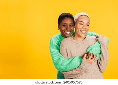 Two young cheerful women wearing green clothes embracing in a studio with a yellow background. - Powered by Shutterstock