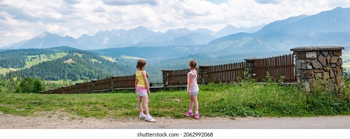 Two Young Children, Elementary Age Girls Standing In Front Of Full Polish Tatra Mountain Range, High Resolution Panorama. Kids Travel And Exploration Lifestyle, Trip Destinations, Europe, Poland.