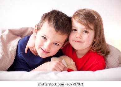 Two Young Children Hugging Under Duvet