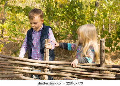 Two young children playing at a rustic wooden fence of interlaced branches with the little girl reaching out to touch the boys arm