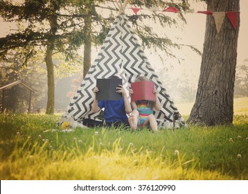 Two Young Children Are Reading Books Together Outside In A Tepee Tent For A Education Or Learning Concept.