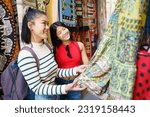 Two young Chinese females visiting Granada, Spain, looking at typical clothes in the typical handicraft stores in the Alcaicer a, old Muslim souk. Concept of Asian people traveling in Europe.