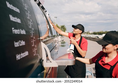 Two young clerks cleaning food truck before opening on sunny morning - Powered by Shutterstock