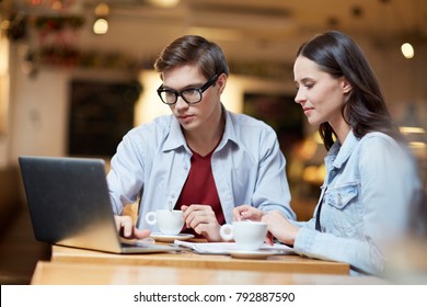 Two Young Colleagues With Laptop Watching Webinar While Sitting In Cafe