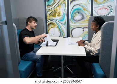Two young colleagues or students in a private meeting booth, candid studying