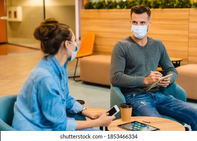 Two Young Colleagues Wearing Medical Masks Talking During Coffee Break In Office