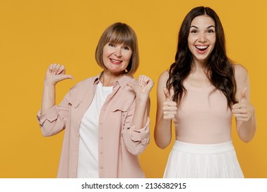 Two young confident happy daughter mother together couple women wearing casual beige clothes point thumb fingers on herself isolated on plain yellow background studio portrait Family lifestyle concept