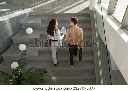 Two young confident managers of high tech company having discussion of working points and online data while going upstairs