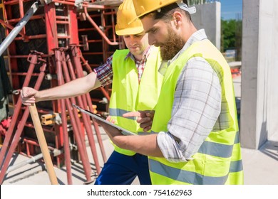 Two young construction workers smiling while using a tablet for online communication through social media during break at work