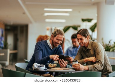 Two young corporate coworkers are socializing on lunch break, using a cellphone to show each other family pictures in the cafeteria. - Powered by Shutterstock