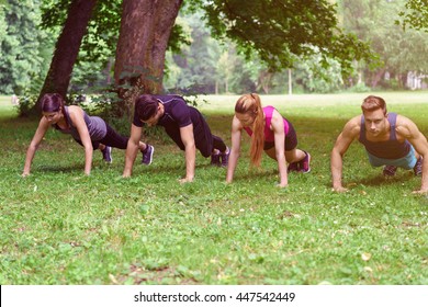 Two Young Couple Working Out In A Park Doing Push-ups Together In A Row As They Enjoy Their Daily Workout