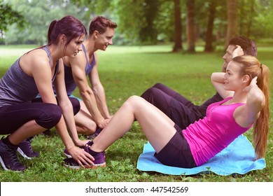 Two young couples doing sit ups in the park with one couple holding down the feet of the second man and woman as they work out in a healthy lifestyle concept - Powered by Shutterstock