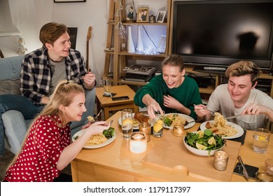 Two Young Couples Are Enjoying A Dinner Party At Home. They Are Eating Homemade Spaghetti Carbonara With Garlic Bread And Salad.