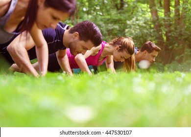 Two young couples working out doing push-ups outdoors in a park with an extreme low angle view across the top of the grass of their heads and shoulders - Powered by Shutterstock