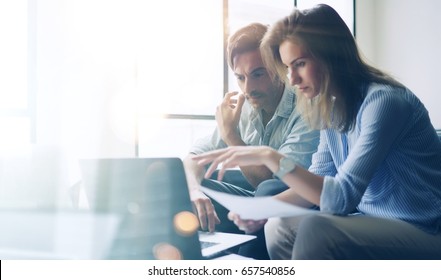 Two young coworkers working on laptop computer at sunny office.Woman holding paper documents and pointing on notebook screen. Horizontal.Blurred background - Powered by Shutterstock