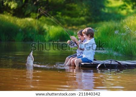 Two young cute boys fishing on a lake in a sunny summer day. Kids are playing. Friendship.