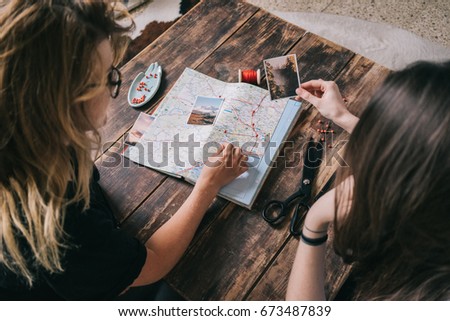 Two young cute girls explore paper map of Europe for new routes for summer trip. Students drop pins  with distances and planning their journey