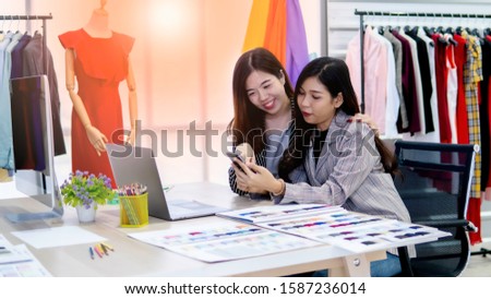 Two young designer happily using smartphone contact customer in the garment store
