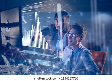 Two young designers are working on a new project in the night office using modern technology with hud display interface - Powered by Shutterstock