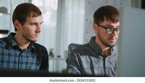 Two young developers working together on a programming project in a well-lit workspace. Collaboration, concentration, and teamwork in tech.