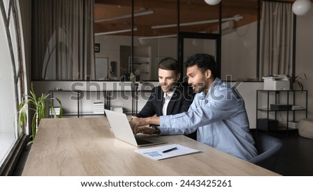 Two young diverse project managers men in casual working on startup at computer, talking at laptop, pointing screen, speaking, discussing online marketing strategy at office workplace. Banner shot