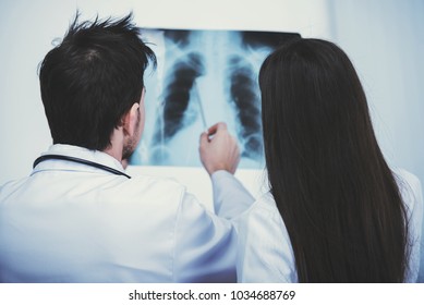 Two young doctors are looking at X-ray in medical office. Back view.
