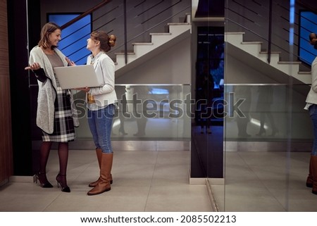 Two young elegant and attractive female colleagues met in the hall and now cheerfully chatting in a friendly atmosphere. Business, inside, work