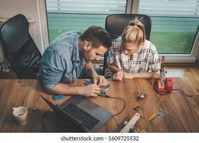 Two young engineers are focused on the repair of electronic equipment and checking something on the laptop.