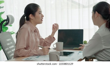 Two young enthusiastic businesswoman working together in the office workspace. Young colleagues having discussion and using laptop together. Modern office workers sitting together at desk. - Shutterstock ID 2233801129