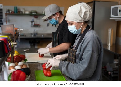 
Two Young Entrepreneurs Cooking And Handling Food With Chinstrap And Gloves For Precaution