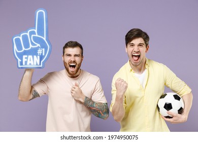 Two Young Excited Fun Men Friends Together In Casual T-shirt Fan Foam Glove Finger Hold Soccer Football Ball Do Winner Gesture Clench Fist Isolated On Purple Background Studio People Lifestyle Concept