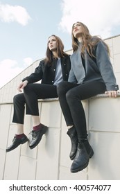 Two Young Fashion Woman Sit On Parapet, Low Angle