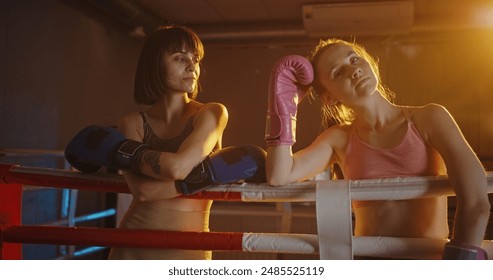 Two young female boxers share an embrace after an intense match, demonstrating sportsmanship and mutual respect in a warmly lit boxing ring - Powered by Shutterstock