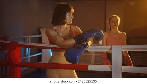 Two young female boxers share an embrace after an intense match, demonstrating sportsmanship and mutual respect in a warmly lit boxing ring - Powered by Shutterstock