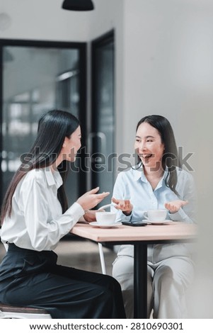 Two young female colleagues talking and laughing during a coffee break in an office.