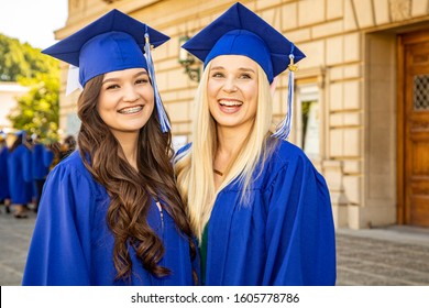 Two Young Female College Or High School Graduates In Blue Cap And Gown Having A Great Time Together At Graduation. One Graduate Is Blonde And The Other Brunette