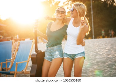 Two Young Female Friends Hangout At The Beach ,singing And Relaxing In Beautiful Summer Sunset.They Hug Each Other.