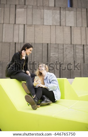 Two young female student sitting outside and having fun. Urban concept