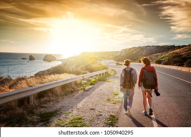 Two young female travel girlfriends walking along a highway, against a background of sunset and sea coast. Travel and freedom, adventures and directions for travel - Powered by Shutterstock