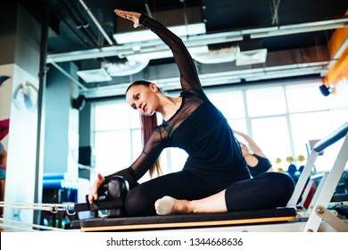 Two young females wearing sports clothing doing reformer exercises on pilates machines indoors in a studio