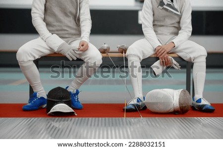 Two young fencers talking while sitting on bench after training