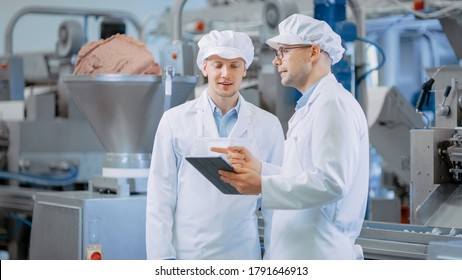 Two Young Food Factory Employees Discuss Work-Related Matters. Male Technician or Quality Manager Uses a Tablet Computer for Work. They Wear White Sanitary Hat and Work Robes. - Shutterstock ID 1791646913
