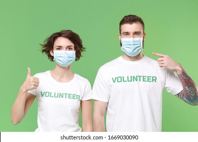 Two young friends couple in volunteer t-shirt isolated on pastel green background. Voluntary free work assistance help charity grace teamwork. Point index finger on sterile face mask showing thumb up - Powered by Shutterstock